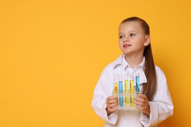 Photo of Little girl with test tubes pretending to be scientist on orange background, space for text. Dreaming of future profession