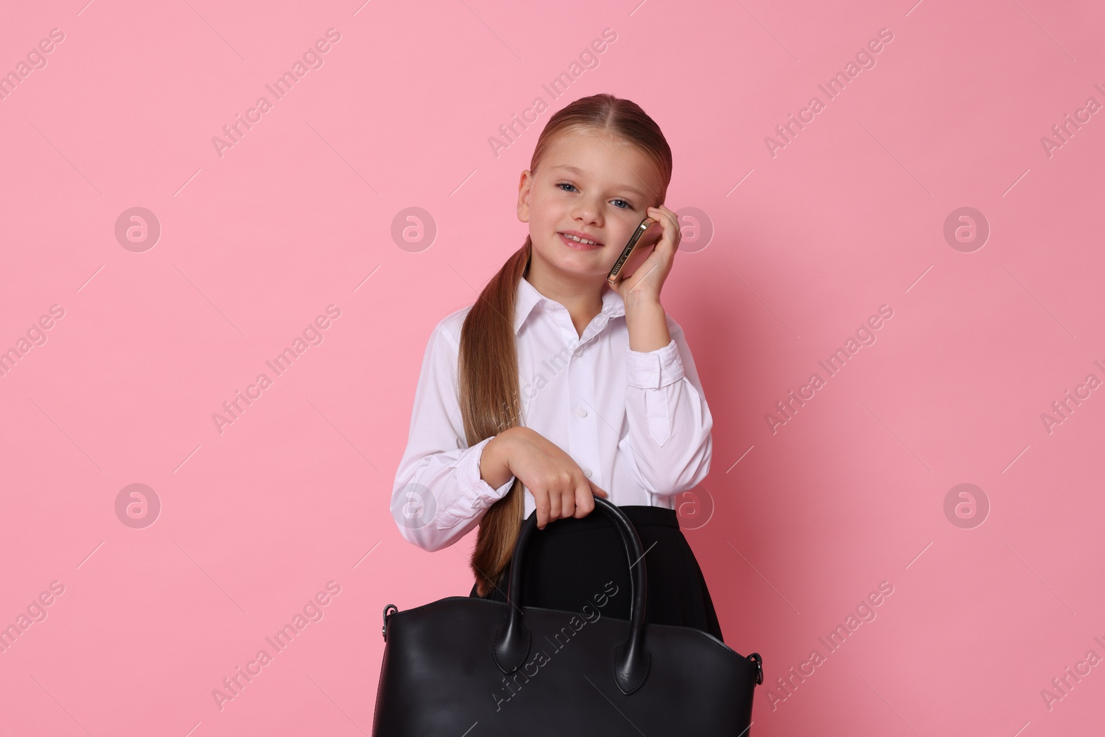 Photo of Little girl with bag talking on smartphone and pretending to be businesswoman against pink background. Dreaming of future profession