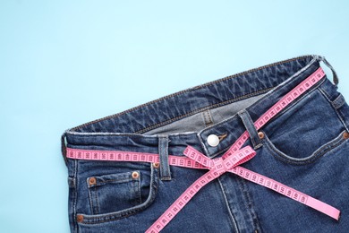 Photo of Jeans and measuring tape on light blue background, top view. Space for text