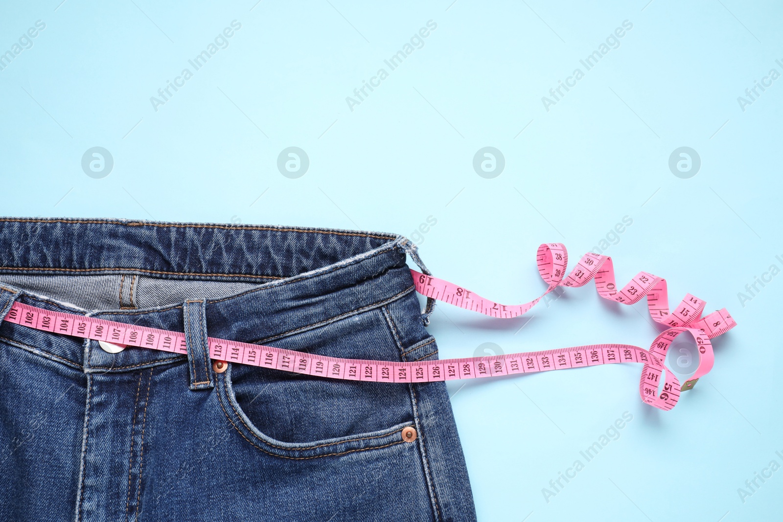 Photo of Jeans and measuring tape on light blue background, top view. Space for text