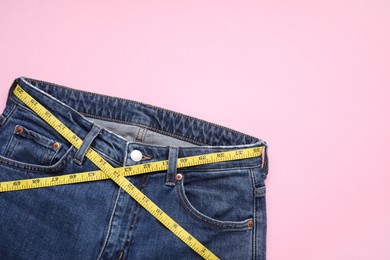 Photo of Jeans and measuring tape on pink background, top view. Space for text