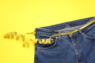 Photo of Jeans and measuring tape on yellow background, top view