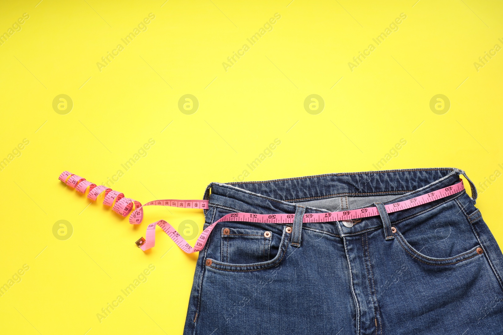 Photo of Jeans and measuring tape on yellow background, top view. Space for text