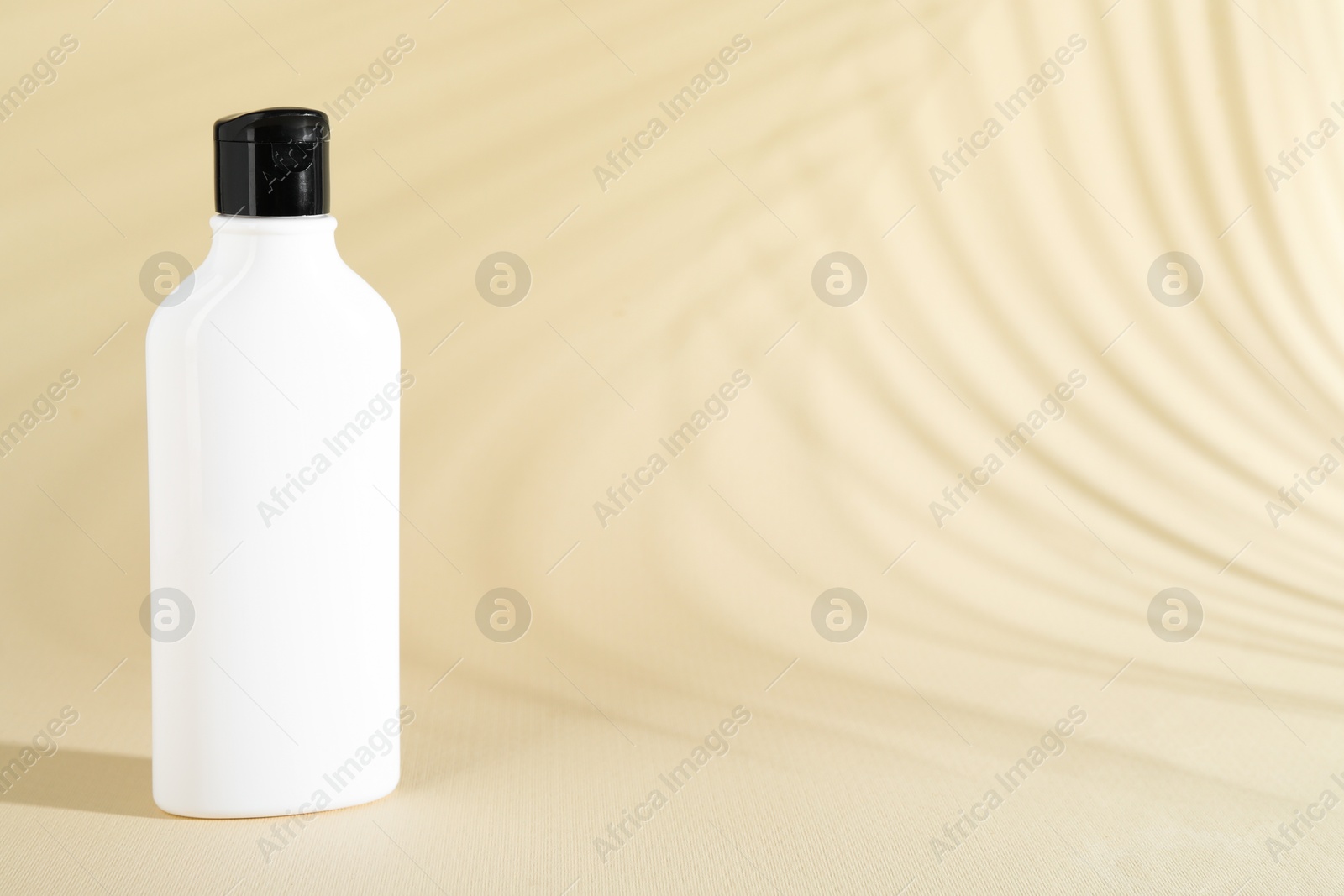 Photo of Shampoo in bottle on beige background, space for text