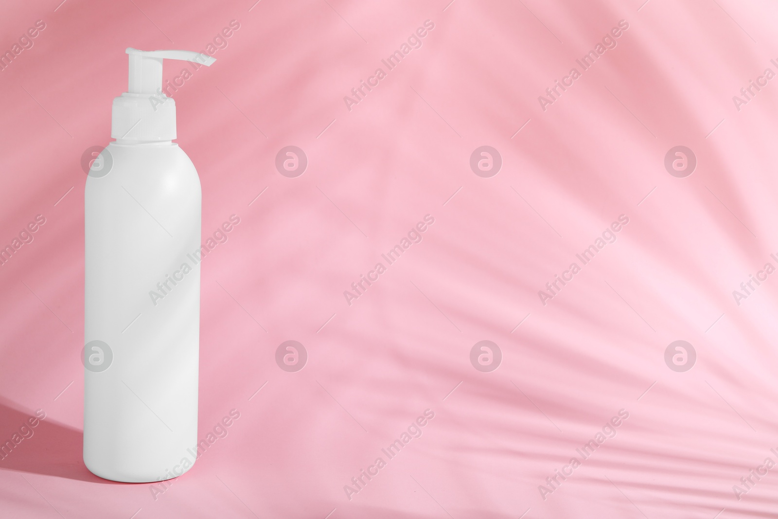 Photo of Shampoo in bottle on pink background, space for text