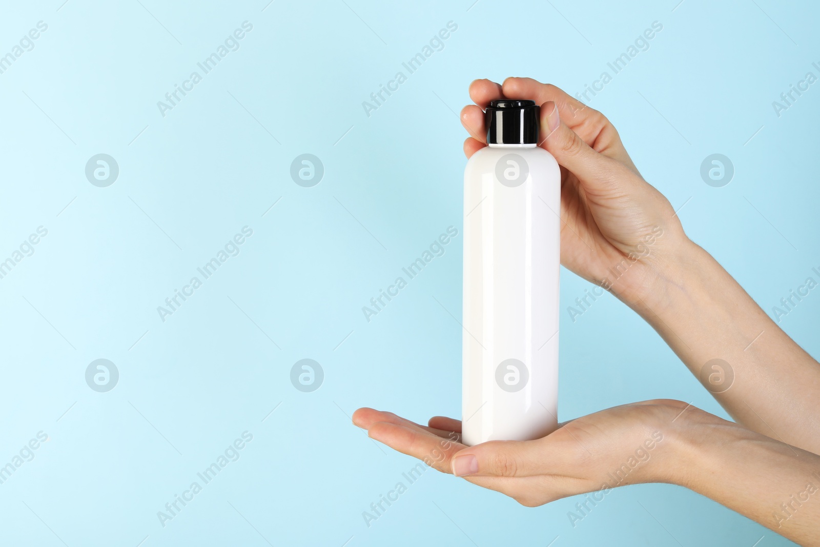 Photo of Woman with shampoo bottle on light blue background, closeup. Space for text