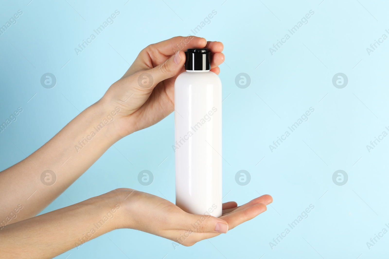 Photo of Woman with shampoo bottle on light blue background, closeup