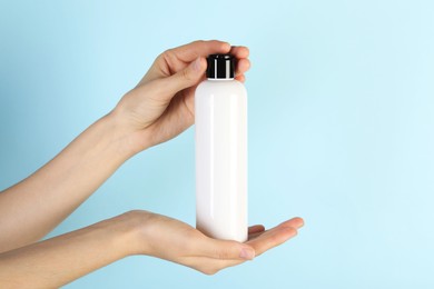 Photo of Woman with shampoo bottle on light blue background, closeup