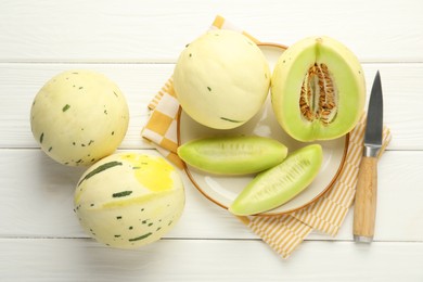 Photo of Fresh whole and cut honeydew melons on white wooden table, flat lay