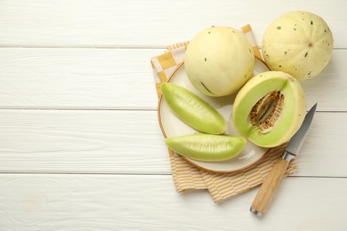 Photo of Fresh whole and cut honeydew melons on white wooden table, flat lay. Space for text