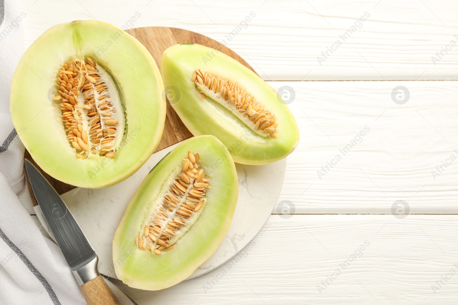 Photo of Fresh cut honeydew melon on white wooden table, top view. Space for text