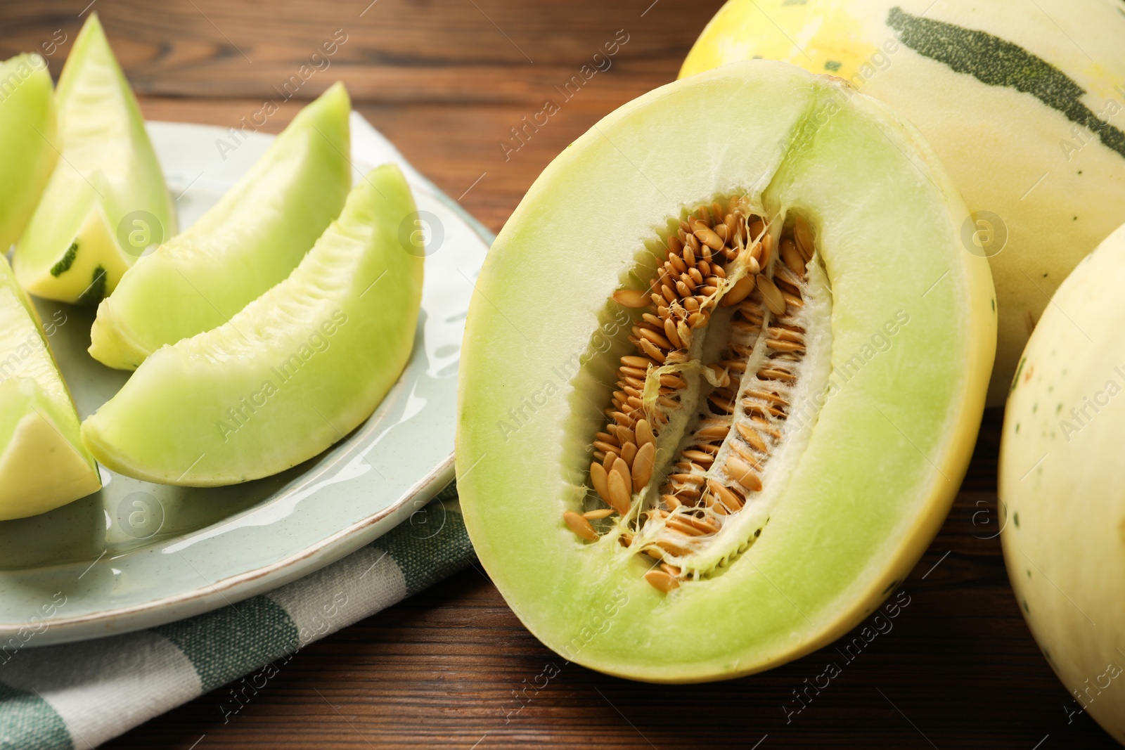 Photo of Fresh whole and cut honeydew melons on wooden table, closeup