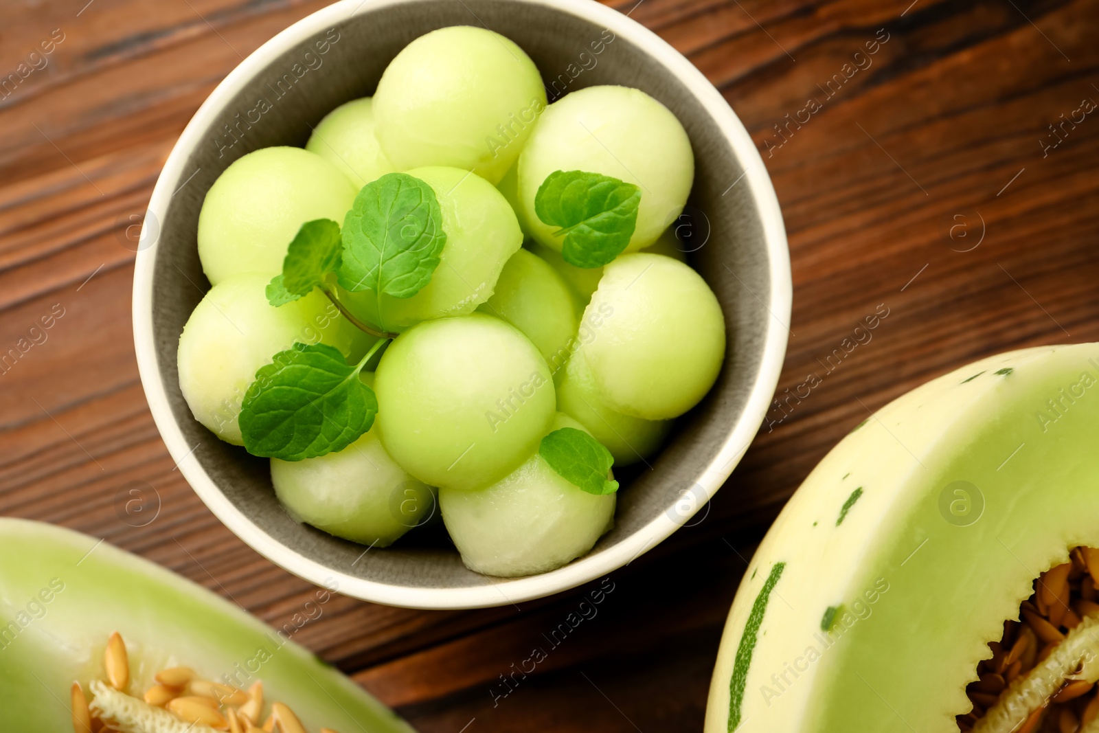 Photo of Melon balls in bowl and fresh fruit on wooden table, flat lay