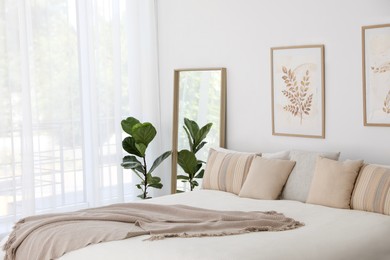 Photo of Large bed, houseplant and full-length mirror near window in room. Stylish bedroom interior