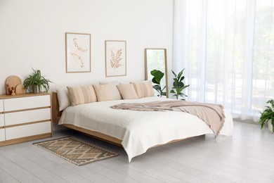 Photo of Large bed, houseplant and full-length mirror near window in room. Stylish bedroom interior