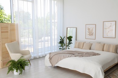 Photo of Large bed, houseplant and full-length mirror near window in room. Stylish bedroom interior