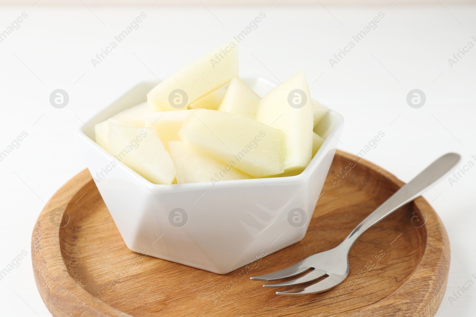 Photo of Cut tasty melon in bowl on white table, closeup