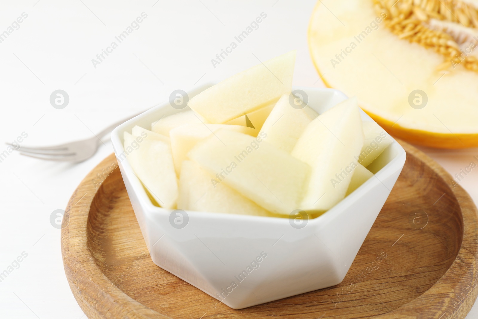 Photo of Cut tasty melon in bowl on white table, closeup