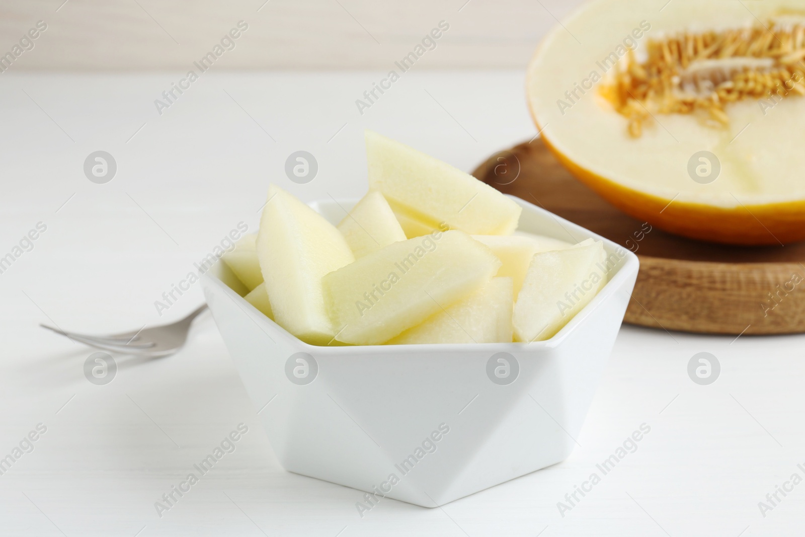 Photo of Cut tasty melon in bowl on white table, closeup