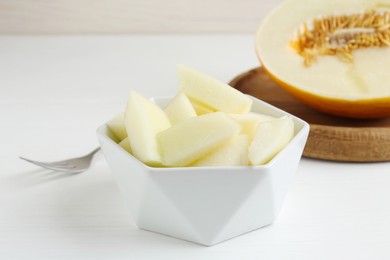 Cut tasty melon in bowl on white table, closeup