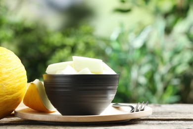 Photo of Cut ripe melon in bowl served on wooden table outdoors, space for text