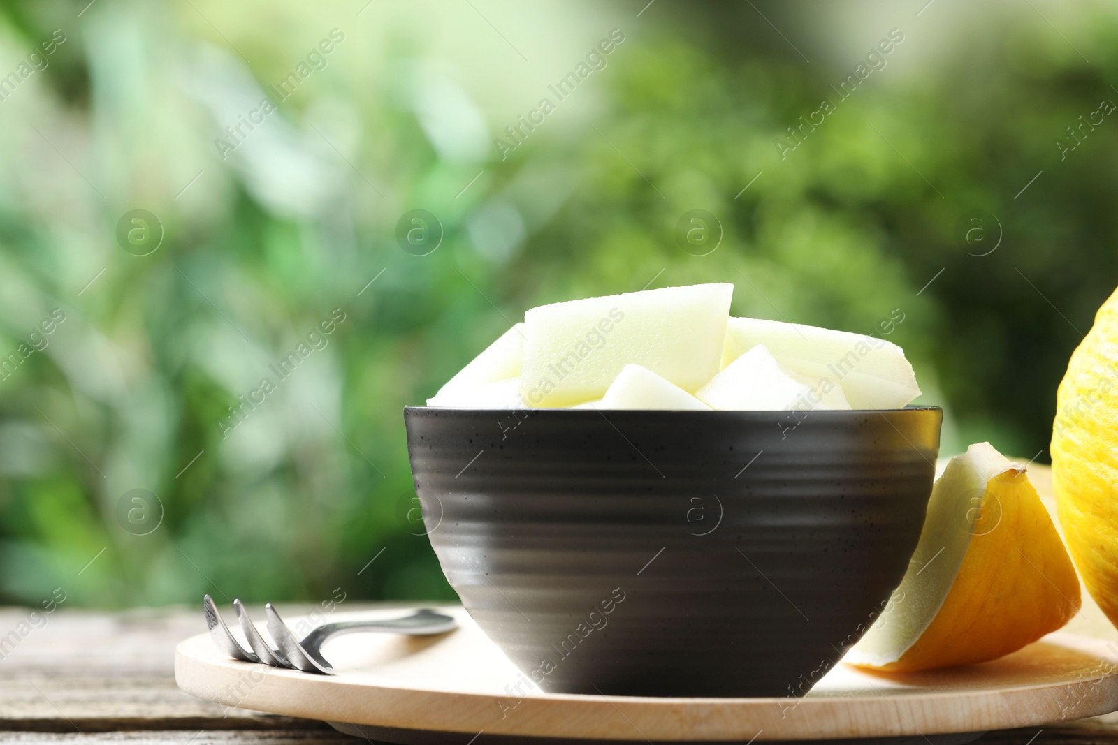 Photo of Cut ripe melon in bowl served on wooden table outdoors, closeup