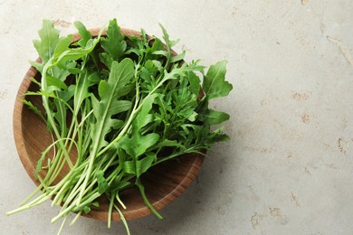 Photo of Many fresh arugula leaves in bowl on grey textured table, top view. Space for text