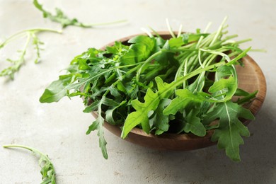 Photo of Many fresh arugula leaves in bowl on grey textured table, closeup