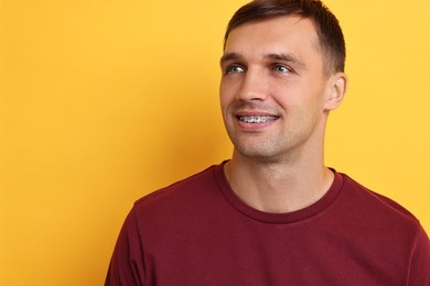 Photo of Smiling man with dental braces on yellow background. Space for text