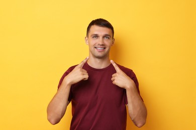 Photo of Smiling man pointing at his dental braces on yellow background