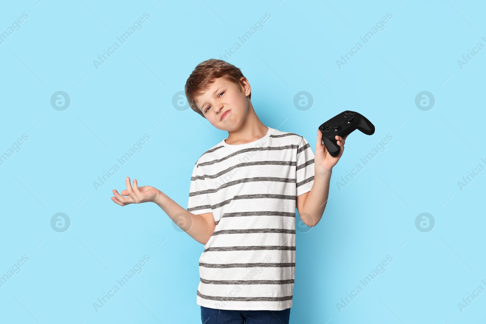 Photo of Cute little boy with controller on light blue background