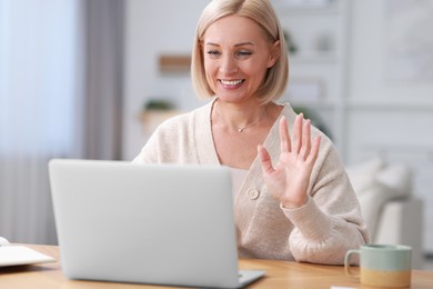 Photo of Happy middle aged woman having video chat via laptop at wooden table indoors