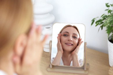 Photo of Smiling woman doing facial self massage near mirror at home