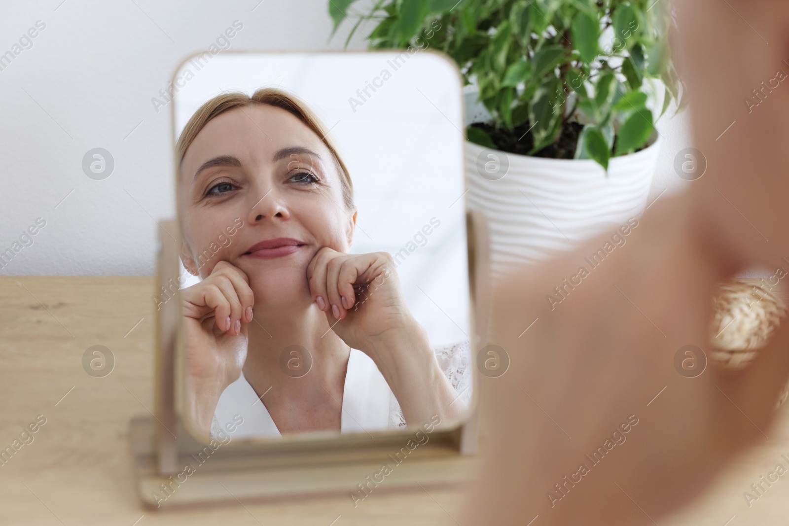 Photo of Beautiful woman doing facial self massage near mirror at home