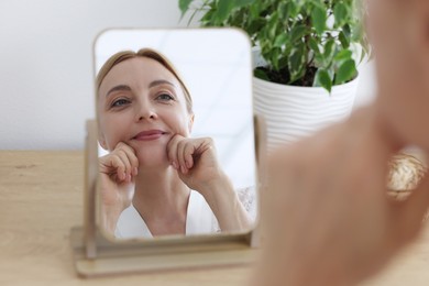 Beautiful woman doing facial self massage near mirror at home