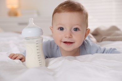 Cute little baby with bottle of milk on bed indoors