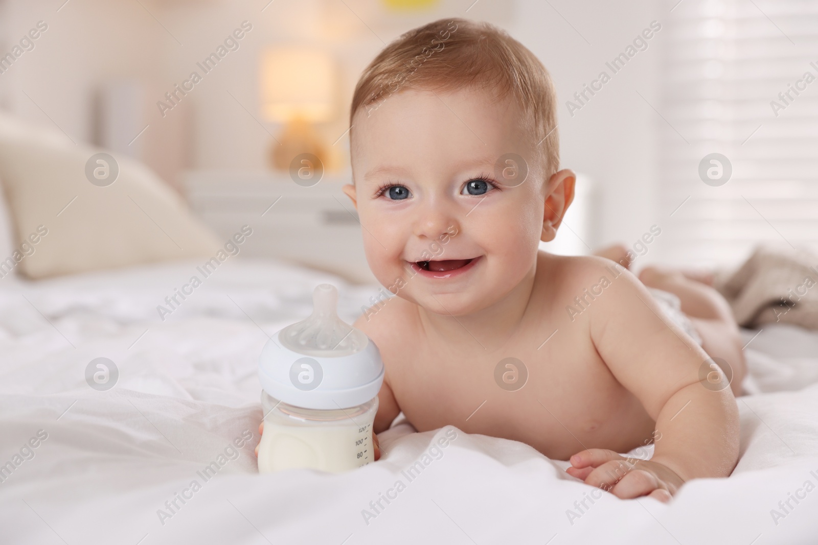 Photo of Cute little baby with bottle of milk on bed indoors