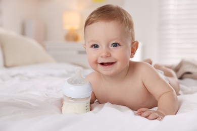 Photo of Cute little baby with bottle of milk on bed indoors