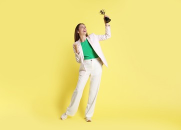 Photo of Happy winner with gold trophy cup on yellow background