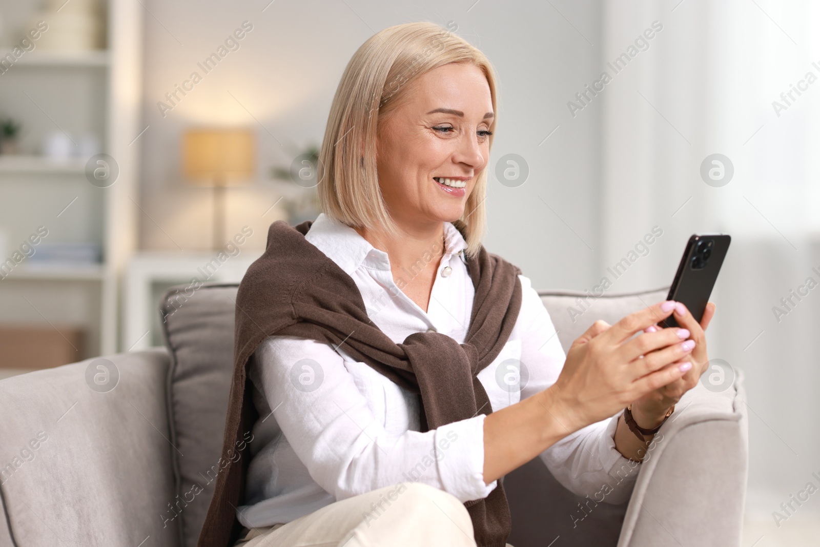 Photo of Smiling middle aged woman using smartphone at home