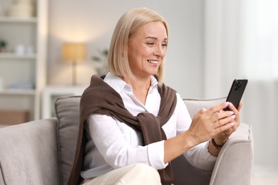 Smiling middle aged woman using smartphone at home