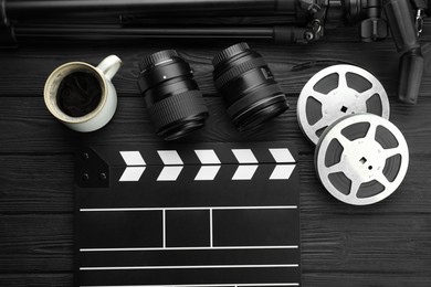 Photo of Movie clapper, camera lens, film reels and cup of coffee on black wooden table, flat lay