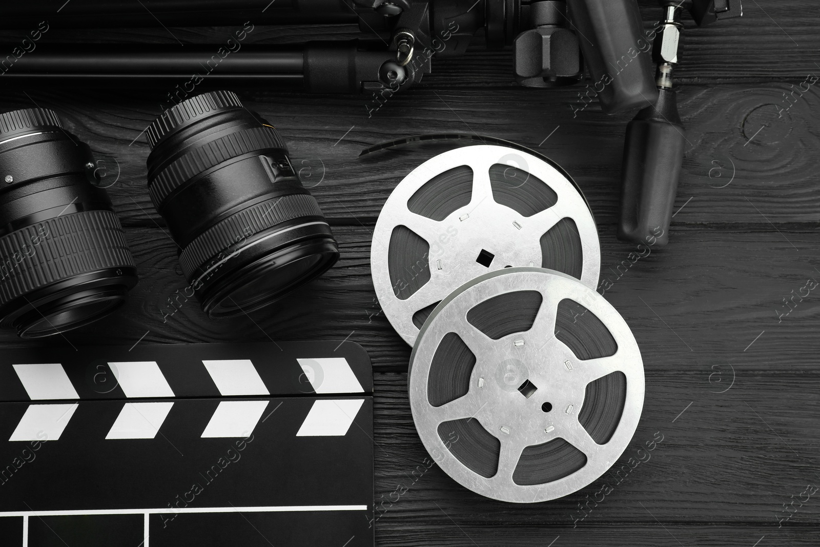 Photo of Movie clapper, camera lens and film reels on black wooden table, flat lay