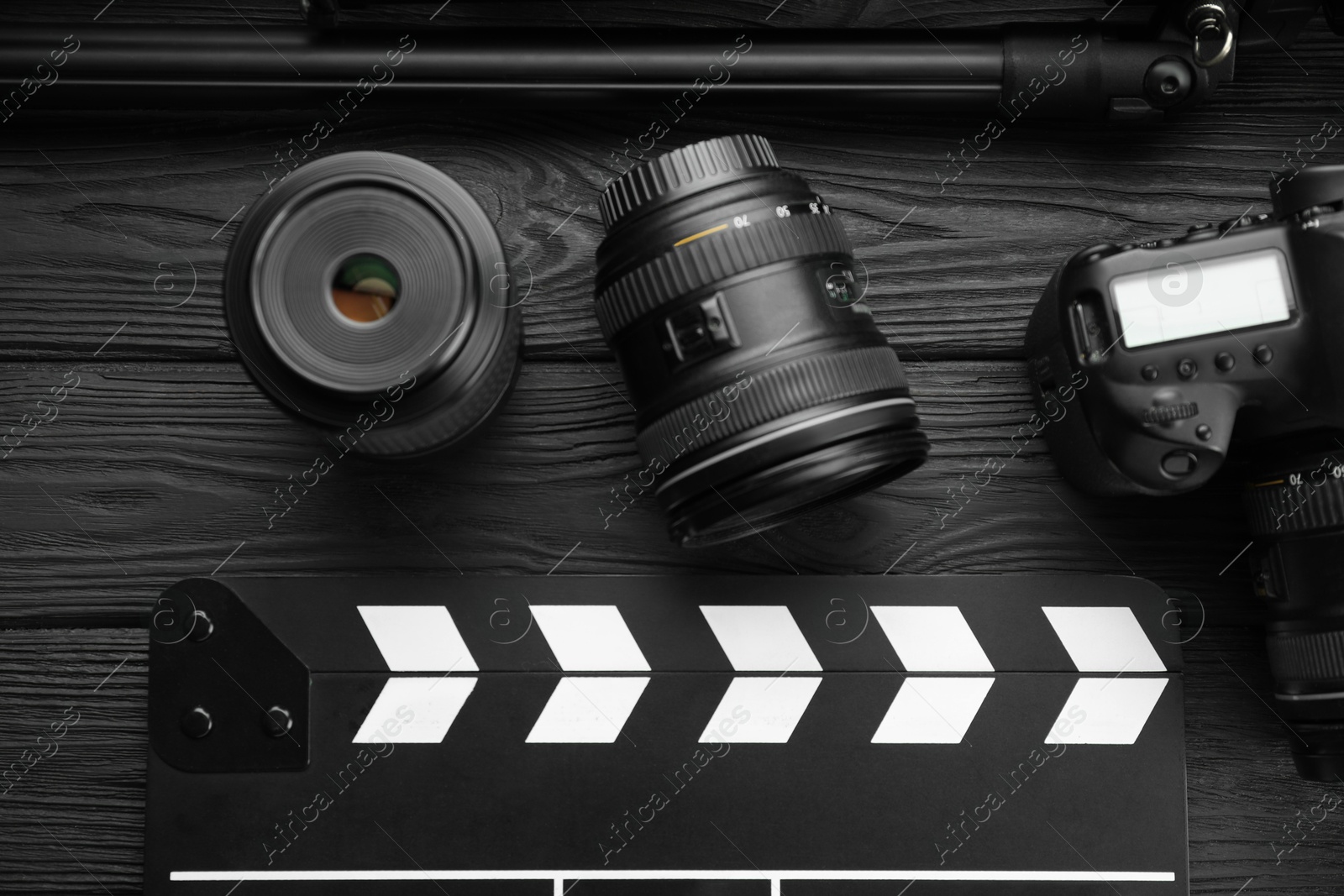 Photo of Movie clapper, camera and lens on black wooden table, flat lay