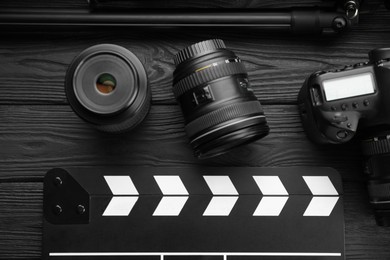 Photo of Movie clapper, camera and lens on black wooden table, flat lay