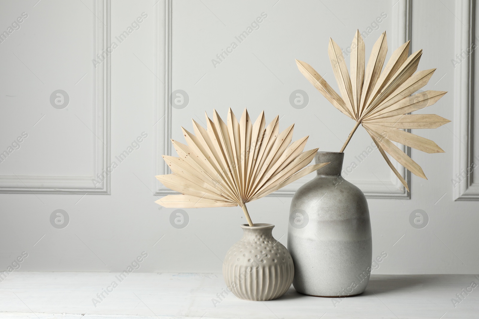 Photo of Stylish vases with dry palm leaves on white table, space for text