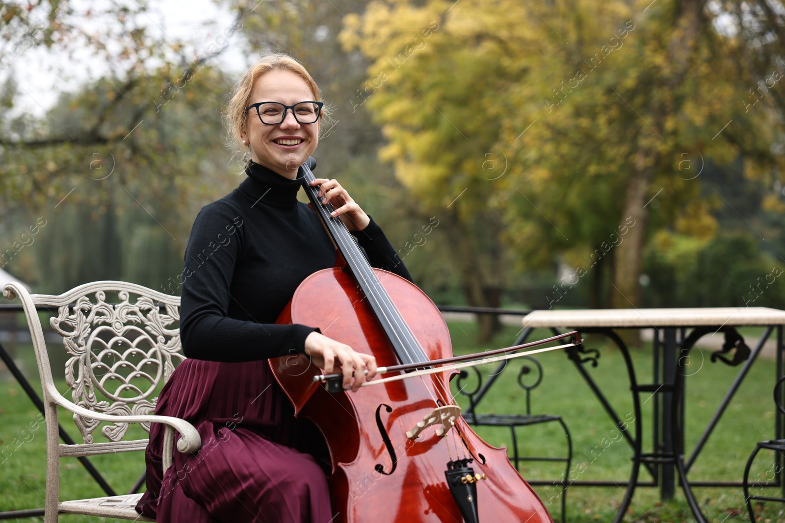 Photo of Beautiful young woman playing cello in park, space for text