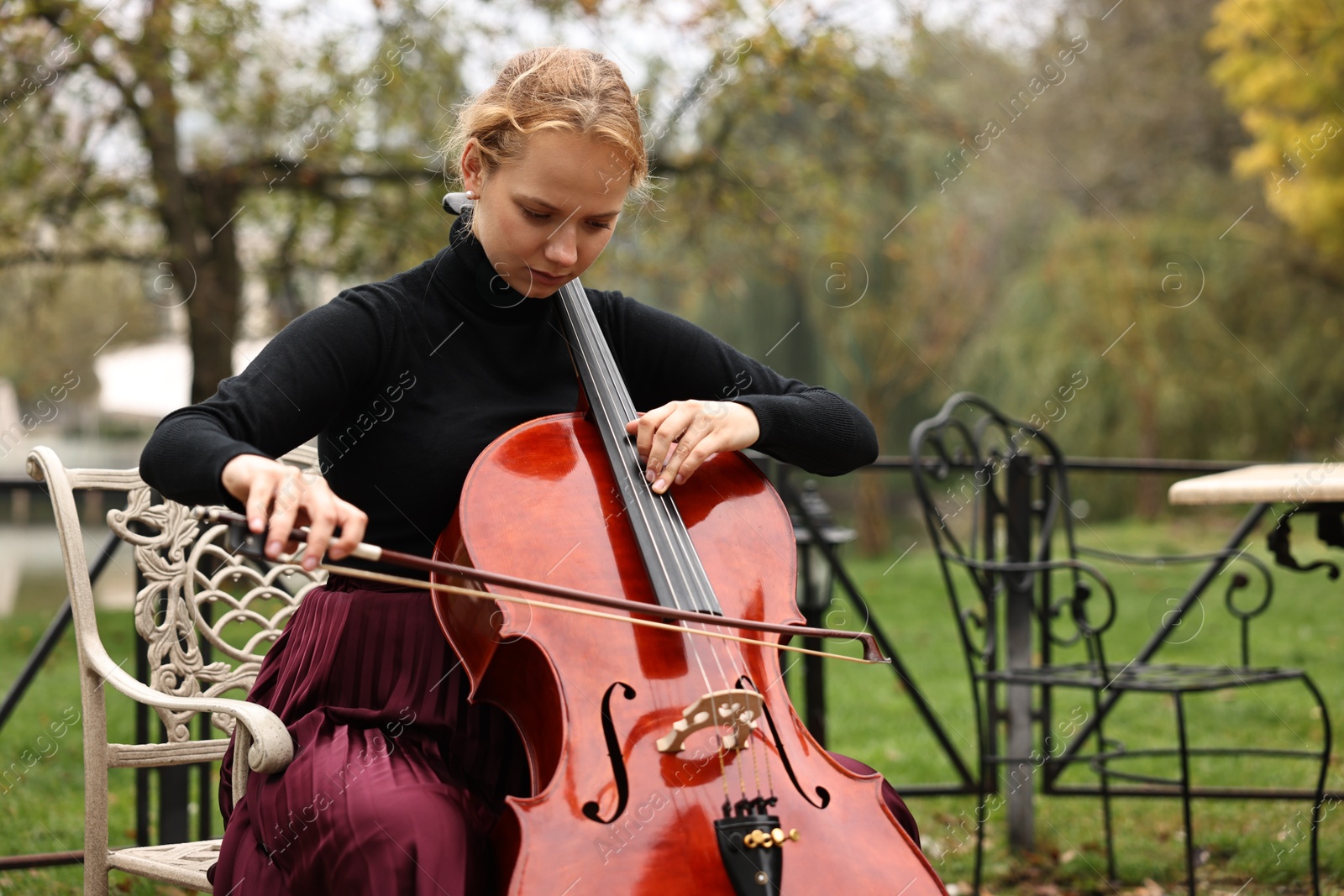 Photo of Beautiful young woman playing cello in park, space for text