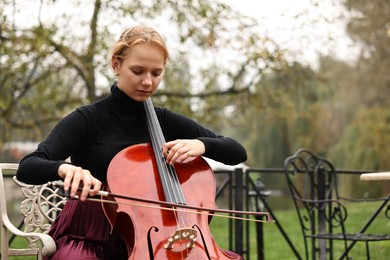 Photo of Beautiful young woman playing cello in park, space for text