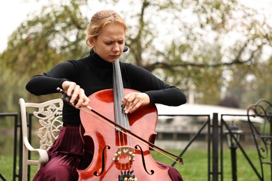 Beautiful young woman playing cello in park, space for text